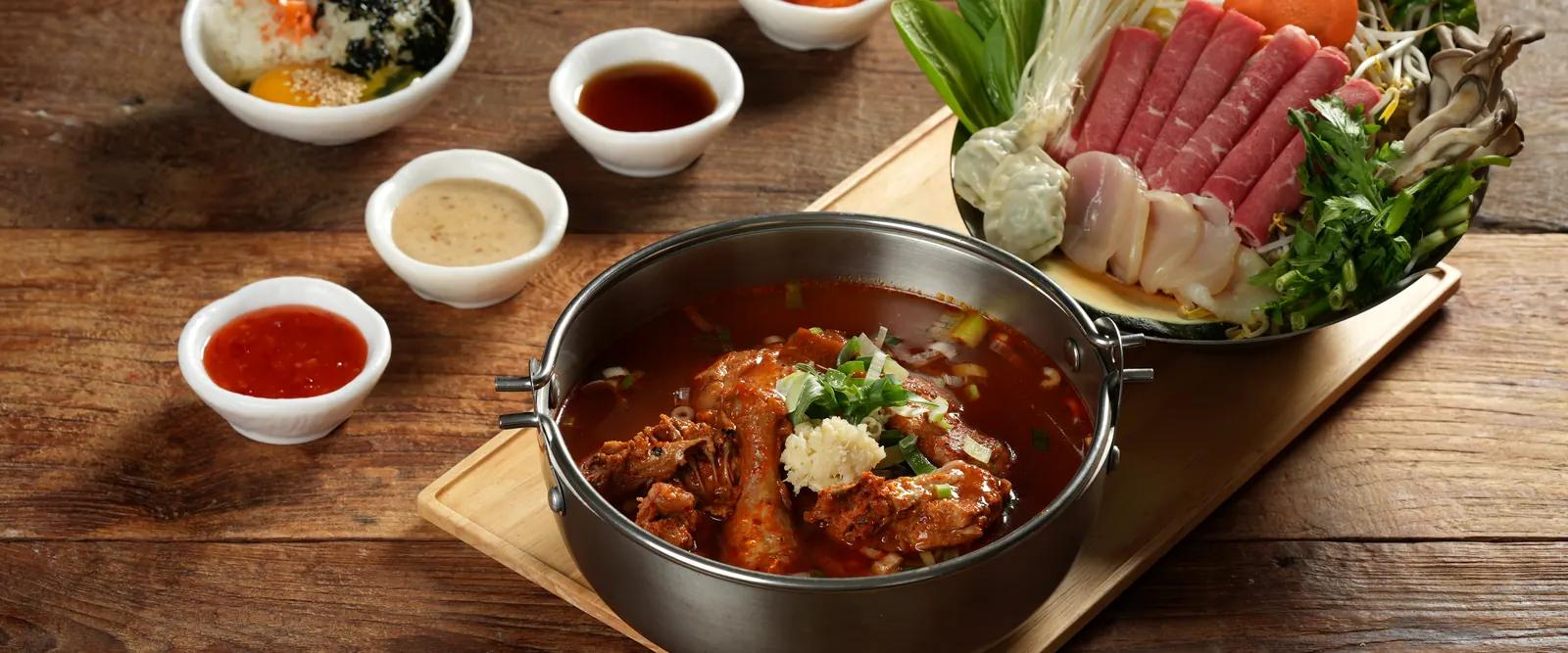 얼큰 닭 육수 냄비와 소고기, 채소, 죽 재료가 차려진 한 상