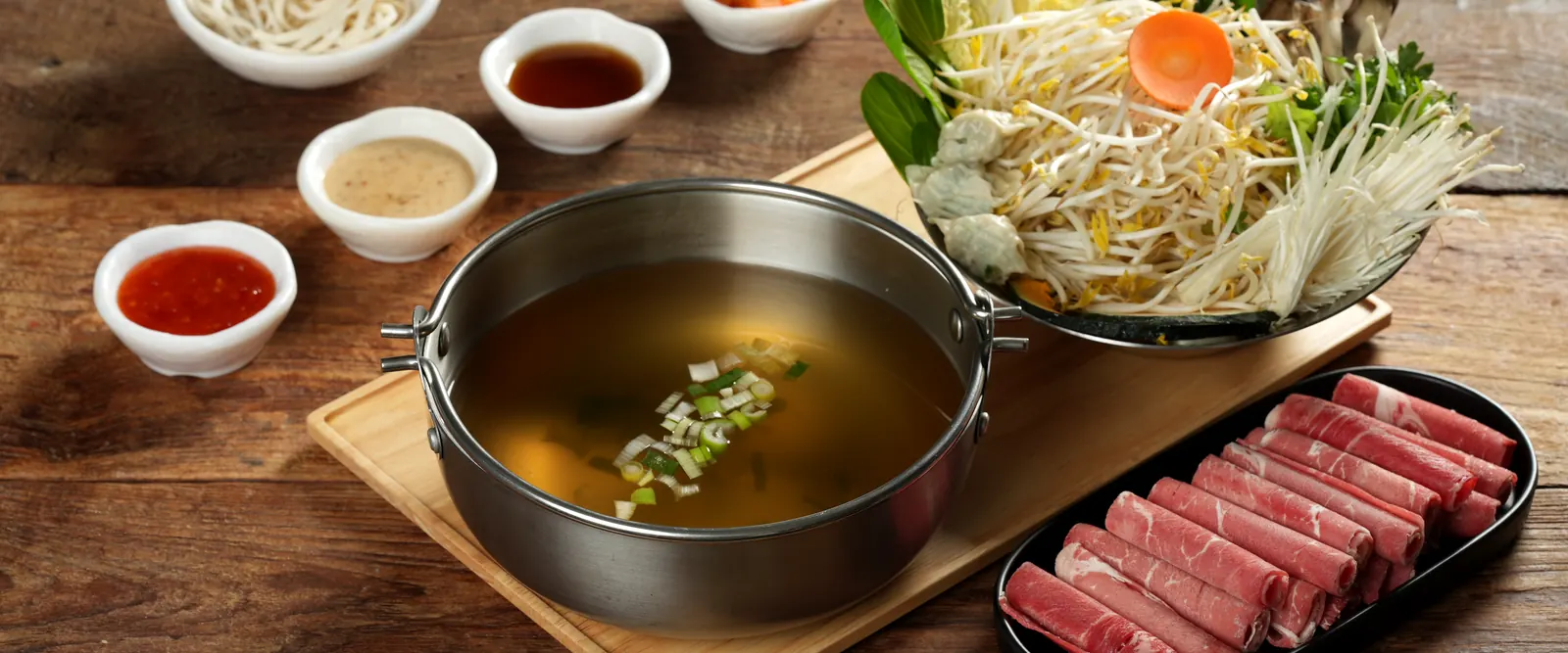 맑은 육수 냄비와 소고기, 채소, 소스가 차려진 한 상
